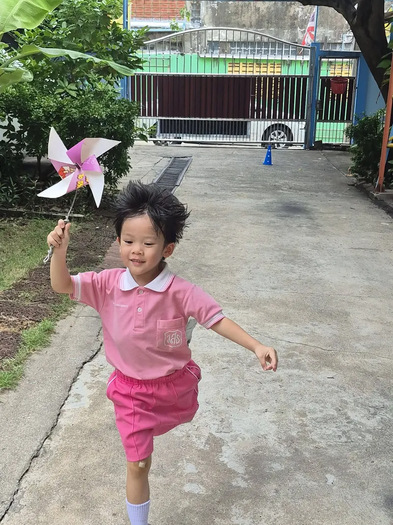 เด็กชายในชุดนักเรียนสีชมพูวิ่งถือกังหันลมในโรงเรียน